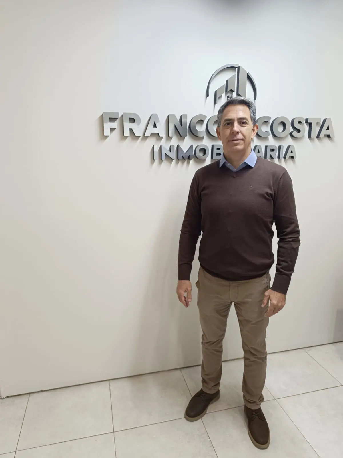 Franco Acosta en la oficina de su inmobiliaria, frente al logo de Franco Acosta Inmobiliaria